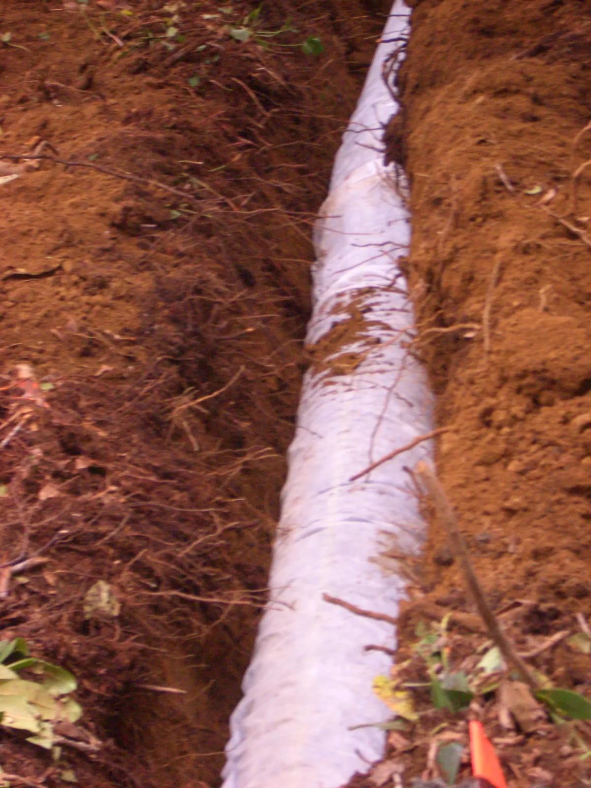 Open trench with perforated drain field pipe laid on a bed of crushed stone before backfilling